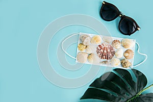Medical face mask, sunglasses and seashells on a blue background. Flat lay, copy space, vacation cancellation, pandemic, tourism
