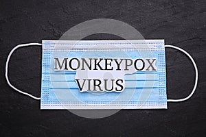 Medical face mask with words Monkeypox Virus on dark background, top view