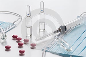 Medical face masks, pink pills, ampullas and expendable syringe for vaccination. Coronavirus vaccination concept. COVID-19