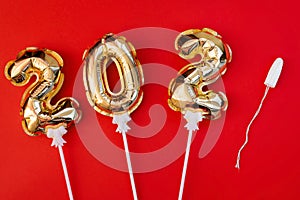 Medical female tampon with gold foil balloons number 2021 on a red background. Hygienic white tampon for women. Cotton swab.