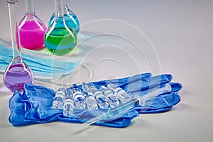 Medical flasks with colorful chemical reagents. Seven mockup ampoules and syringe on blue disposable gloves, mask