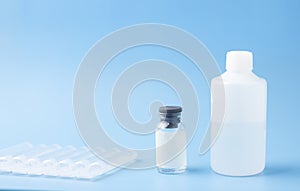 Medical glass bottle with copy space, on a blue background next to ampoules and a plastic bottle with saline solution, medicine.