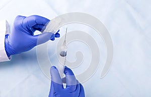 Medical gloved hands holding syringe with a bead of liquid emerg