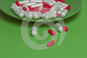 medical green background.Capsules of red and white flowers pour out from a green plate on a green background.