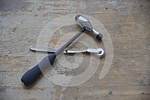 A medical hammer and a Wartenberg wheel lie on a gray wooden surface.