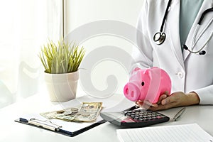 Medical and health insurance concept, Doctor holding piggy bank and money in hospital background.