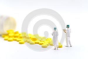 Medical and Healthcare Concept. Closeup two doctor miniature with patients file standing with yellow pills with bottle on white