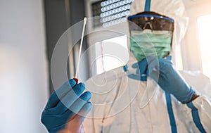 Medical healthcare technologist holding COVID-19 swab collection kit, wearing white PPE protective suit mask gloves, test tube for