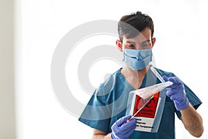 Medical healthcare technologist holding COVID 19 swab collection kit, wearing white protective suit mask and gloves