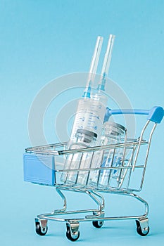 Medical injection in shopping trolley on blue background. Creative idea for health care cost, drugstore, health insurance and