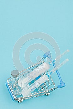 Medical injection in shopping trolley on blue background. Creative idea for health care cost, drugstore, health insurance and