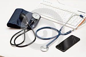 Medical items: blood pressure cuff, stethoscope, telephone keyboard on a wooden table. Online doctor