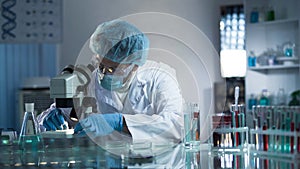 Medical lab worker examining laboratory glass with sample through microscope