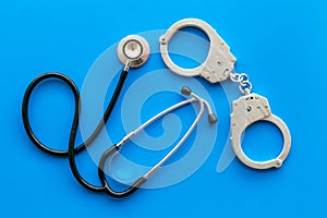 Medical lawsuit. Arrest for medical crime concept. Handcuff near stethoscope on blue background top view