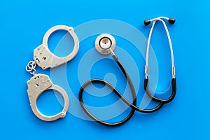 Medical lawsuit. Arrest for medical crime concept. Handcuff near stethoscope on blue background top view