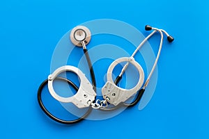 Medical lawsuit. Arrest for medical crime concept. Handcuff near stethoscope on blue background top view