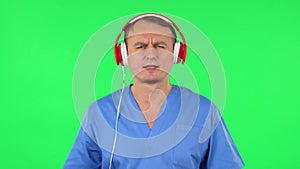 Medical man dancing and singing in big red headphones. Green screen