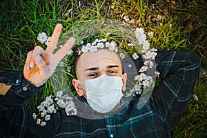 Medical mask as protection against coronavirus. guy lies on grass around early spring flowers
