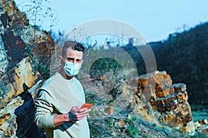 Medical mask as protection against coronavirus. guy in the mountains isolated from coronavirus. looking at his phone