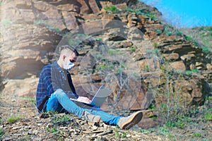 Medical mask as protection against coronavirus. guy in the mountains isolated from coronavirus. works on laptop