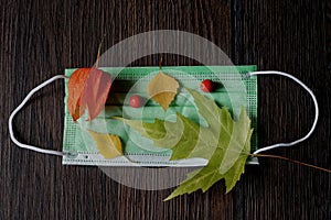 Medical mask with autumn leaves on a dark background photo