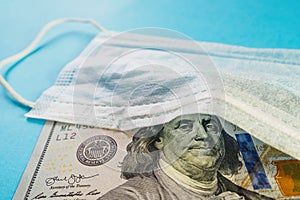 Medical mask and banknote of 100 dollars on blue background. Concept of deficit, speculation and sold out of face masks