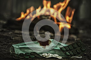 Medical mask with blood stain. Pills near the mask. In the background, fire burns infected things concept of a deadly disease