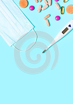 Medical mask, electronic thermometer, pills or vitamins on blue background flat lay top view copy space. Protection against virus