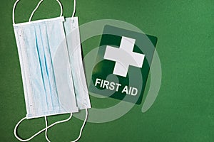 Medical mask and first aid sign on green background