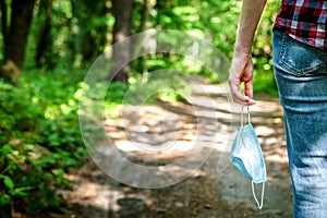 Medical mask in a girl`s hand against the background of a summer forest.