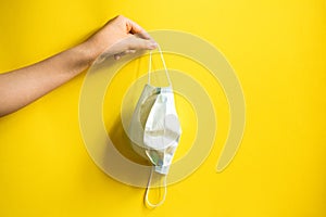 Medical mask in a girl`s hand. Yellow background