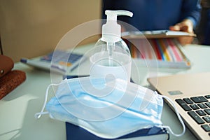 Medical mask and hand disinfectant on table in home office