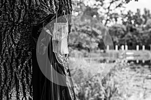 Medical mask hanging on the background of a trash bag on a tree bitch. Close-up. Selective focus. Black and white photo