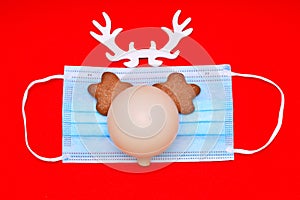 Medical mask with horns and eyes and cookies. nose in the form of a Christmas tree toy on a red background