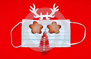 Medical mask with horns and eyes and cookies. nose in the form of a Christmas tree toy on a red background