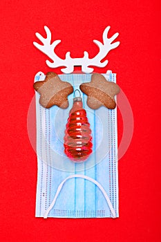 Medical mask with horns and eyes and cookies. nose in the form of a Christmas tree toy on a red background