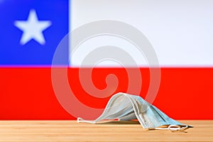 A medical mask lies on the table against the background of the Chilean flag.