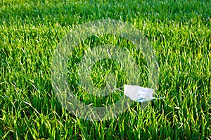 Medical mask lying on the green grass. Used contaminated garbage is released into the environment during the pandemic of the