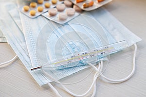 Medical mask and a mercury thermometer - close-up on the table. Means of protection from the cold and flu season