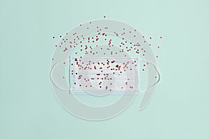 A medical mask on a mint background sprinkled with red sparkles on top, similar to particles of a virus flying around us. Flat lay