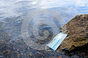 Medical mask on a stone in a pond. the mask was washed ashore by the current