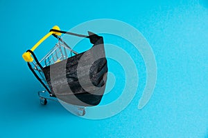 Medical mask and supermarket trolley for shopper on blue paper background. Covid 19 quarantine restrictions concept
