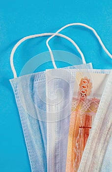 Medical masks and banknote of 5000 rubles on blue background. Concept of deficit, speculation and shortage of face masks