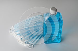 Medical masks and bottle of antiseptic gel on gray background