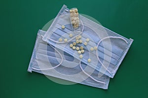 Medical masks on a green background with scattered pills