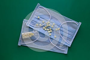 Medical masks on a green background with scattered pills