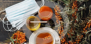 Medical masks with sea buckthorn branches on a dark wooden natural table.The idea of protecting and treating influenza with folk