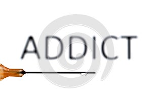 A medical needle with a droplet suspended refracting the word addict, which is also out of focus in the background