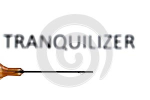 A medical needle with a droplet suspended refracting the word tranquilizer, which is also out of focus in the background