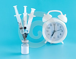 Medical needles stuck in the bottle with the vaccine, alarm clock. Vaccination against the flu, infections, covid-19